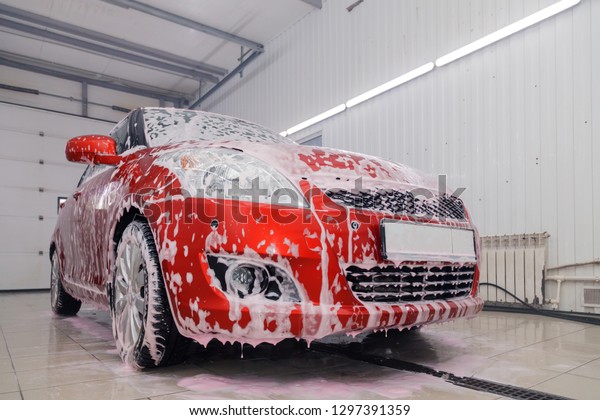 Russia Kemerovo 2019-01-05 Suzuki Swift bright red\
small car at car wash in white foam, professional chemistry for\
cleaning auto. Concept comprehensive care for the exterior and\
interior of car