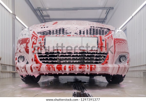 Russia Kemerovo 2019-01-05 Suzuki Swift bright red\
small car at car wash in white foam, professional chemistry for\
cleaning auto. Concept comprehensive care for the exterior and\
interior of car