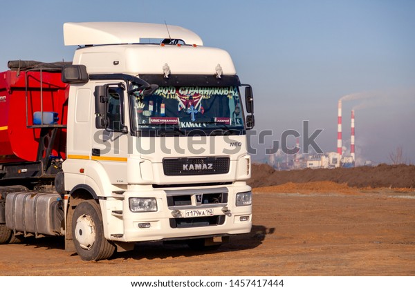 Russia\
Kemerovo 2019-04-09 red and white model Kamaz on field on\
background of the city landscape and factory pipes. Concept truck\
on Rally Dakar in desert. Scale model in\
sand