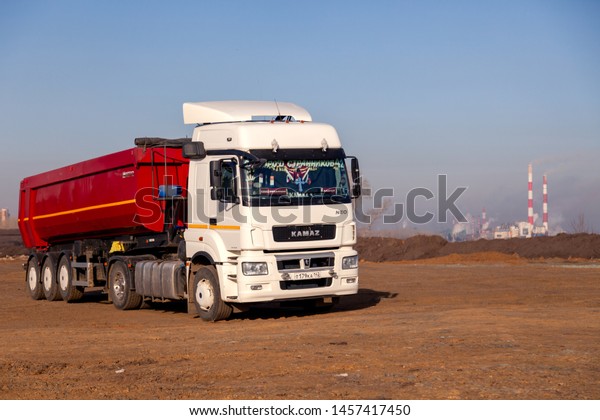 Russia\
Kemerovo 2019-04-09 red and white model Kamaz on field on\
background of the city landscape and factory pipes. Concept truck\
on Rally Dakar in desert. Scale model in\
sand