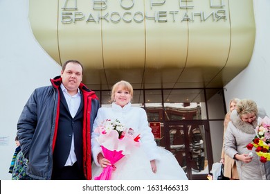 Russia, Kirov - January 24, 2019: Bride And Big Fat Groom After Wedding And Marriage Registration Near Registry Office And Guests And Relatives Meeting Them With Rose Petals In An Autumn Or Winter Day