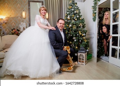 Russia, Kirov - January 24, 2019: Bride And Big Fat Groom Having Fun Before Or After Wedding And Marriage Ceremony And Two Bridesmaids Looking On Them In The Room With Christmas Tree