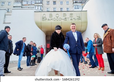 Russia, Kirov - March 22, 2019: Bride And Big Fat Groom After Wedding And Marriage Registration Near Registry Office And Guests And Relatives Meeting Them With Rose Petals In An Autumn Or Winter Day