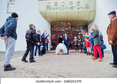 Russia, Kirov - March 22, 2019: Bride And Big Fat Groom After Wedding And Marriage Registration Near Registry Office And Guests And Relatives Meeting Them With Rose Petals In An Autumn Or Winter Day