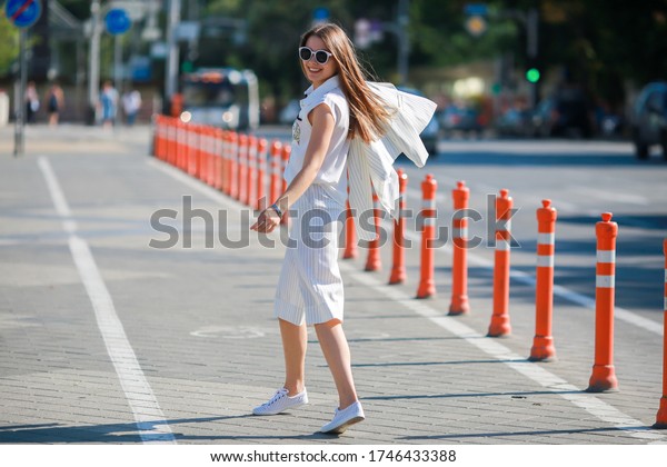 Russia, Krasnodar, 07.04.2016 a Beautiful girl with long\
hair in white shorts, jacket and blouse, and white sneakers, with a\
fashionable small bag \