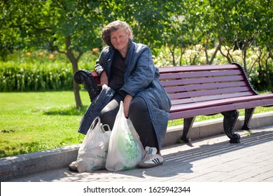 Russia Moscow 2019-06-17 Old Sad Woman Sitting On Bench With Plastic Bags In Summer Park Outdoors. Aged Homeless Woman Feeling Hungry And Sitting Alone Outside.