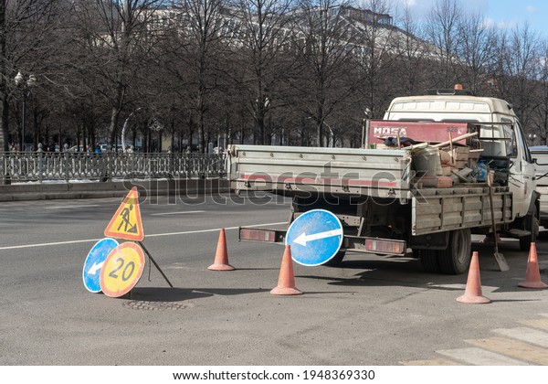 Russia, Moscow - March 28 2021: Road accident signs\
around the car of the road construction crew. Repair and\
engineering works in the\
city.
