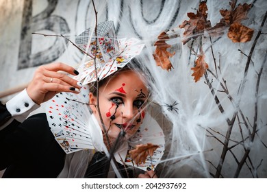 Russia Moscow October 30, 2019 Portrait Of Young Woman With Spooky Makeup Wearing Queen Of Hearts Costume With Card Collar Looking Through Spider Web While Visiting Night Halloween Party