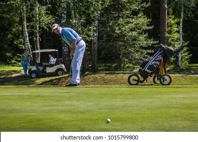 Russia Moscow Region Nakhabino 05.31.2016 Set Of Golf Clubs In A Golf Bag With Green Grass. The Car, Caddy, Forest And Old Man Playing Golf On A Golf Course With Gorgeous Green As Background. 