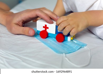 Russia, Moskow - 31 March 2020: Hand Of An Adult And A Child Holding A Wooden Ambulance Toy On A Medical Mask On 31 March, 2020