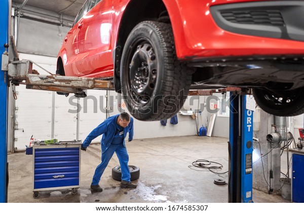 Russia, Nizhny Novgorod - march 13, 2020: Best\
way Auto service. Auto mechanic changes the brakes on the car.\
Rusty drum brakes, rear on red car. Change the old to new brake\
disc on car in a\
garage.