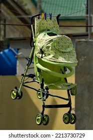 Russia, North-Eastern Caucasus. Derbent. A Green Baby Stroller After Washing Hangs On Clothespins On A Clothesline In One Of The Many Small Courtyards In The City Center.