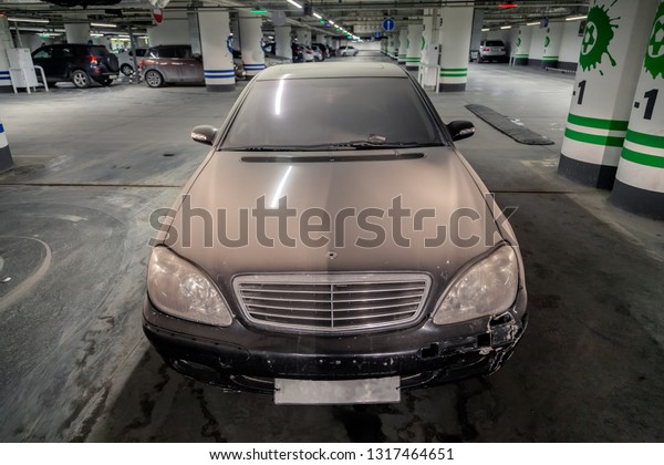 Russia, Novosibirsk, 2019-02-11. Black dusty\
abandoned Mercedes Benz sedan with broken air suspension stands in\
underground parking lot of shopping center. Concept of hacking and\
carjacking