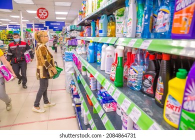 Russia Polevskoy July 2021: A Mature Woman With A Shopping Cart Stands Near A Shelf With Cleaning Products In A Store. Russian Text: Stationery, Cosmetics, Household Chemicals.