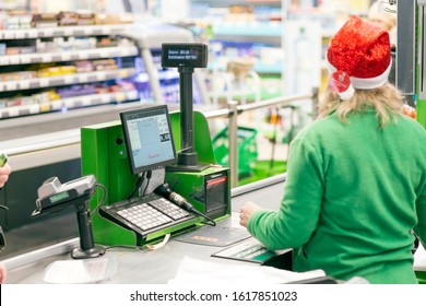 Russia, Samara, December 2019: Cashier Of A Supermarket. A Girl In A Green Uniform And A Christmas Hat Is Standing At The Checkout. Text In Russian: Chocolate Bar, Subtotal, Payment, Use A Pin Pad