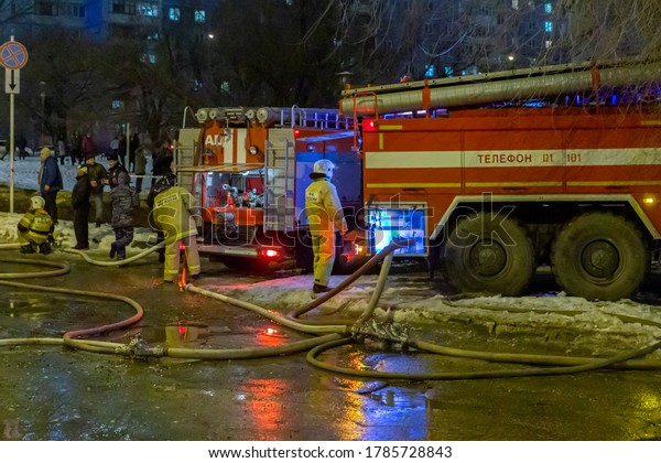 Russia Samara January 2020: Fire trucks in work\
to extinguish a fire in winter at night. Text in Russian: EMERCOM\
of Russia Phone Fire\
brigade