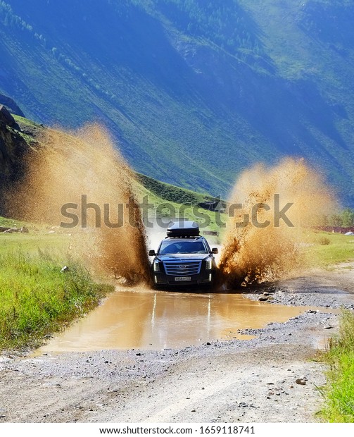 RUSSIA,\
SIBERIA, MOUNTAIN ALTAI  - AUGUST 12.2019: Black SUV storms a deep\
puddle in the Altai mountains at high\
speed