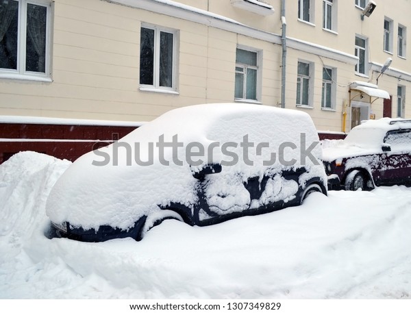 Russia, snowfall. Cars in the yard covered with a large\
snowdrift. 