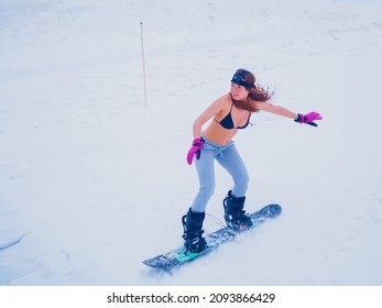 Russia, Sochi 11.05.2019. A Beautiful Girl In A Black Swimsuit And Gray Sweatpants With A Go Pro Camera On Her Head Is Quickly Riding A Snowboard Down The Slope. Krasnaya Polyana