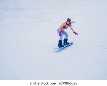 Russia, Sochi 11.05.2019. A Beautiful Girl In A Swimsuit With A Go Pro Camera On Her Head Is Quickly Riding A Snowboard Down The Slope. Krasnaya Polyana