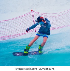 Russia, Sochi 11.05.2019. A guy in shorts with a go pro camera on his head crosses a pool of water on a snowboard. Snowboard competition on the water in the Krasnaya Polyana ski resort.