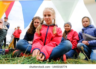 Russia, Tyumen, 15.06.2019. A Crowd Of Children Of Different Ages And Races Sitting On The Grass, Looking At The Camera