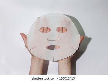 Russia, Udachny, 09/10/2019. Female hands hold a fabric sheet mask for the face. On a white background. View from above.