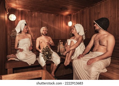 Russian bathhouse. Two couple relaxing and sweating in wooden sauna with hot steam. Four person with bath besoms resting on bench in spa complex. Wellness, self care, healthy concept. Copy text space