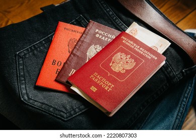 Russian Documents And Cash Money Are Lying On A Stick Of Things, The Man Is Going To Leave Russia So As Not To Participate In The War. Translate: Russian Federation Passport, Military Ticket.