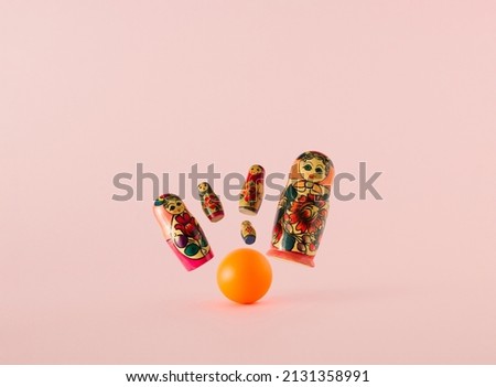 Russian dolls known as matryoshka or babushka as the pins knocked by the orange bowling ball on a pink background. Minimal concept.