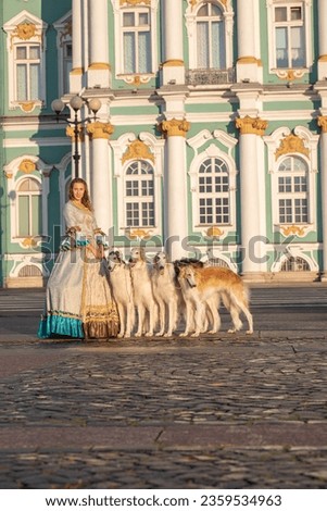 Russian Elegance: A lady in Tsarist-era attire with purebred Borzoi dogs on Palace Square, St. Petersburg, against the Hermitage façade at sunrise
