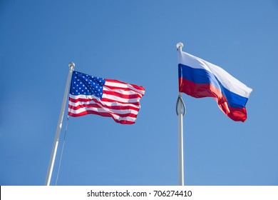 Russian Federation And USA United States Of America Flags On A Blue Sky Background. Idea Of The Sanctions War Combat Negotiation And Confrontation. US And Russia Flag