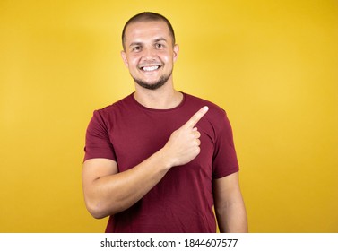 Russian man wearing basic red t-shirt over yellow insolated background smiling and pointing to the side with thumb up.