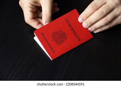 Russian Military ID In Male Hands On Wooden Table. Translation Of Inscription Military ID Card, Russian Federation. Concept Of Mobilization In Russia