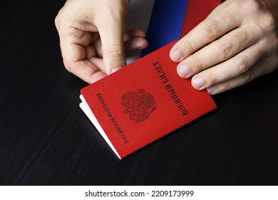 Russian Military ID In Male Hands On Wooden Table. Translation Of Inscription Military ID Card, Russian Federation. Concept Of Mobilization In Russia