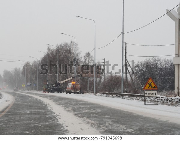 Russian road maintenance service works on M-5\
highway in the Yekaterinburg suburbs under snowfall, using car with\
orange flashing light