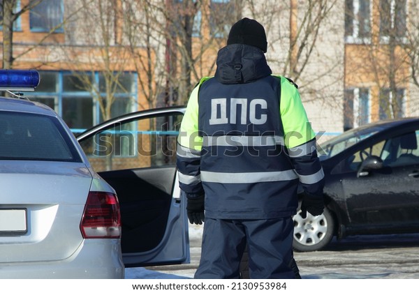 Russian road police man with inscription DPS on\
uniform on work near police car with blue flashlight at winter day\
in the city