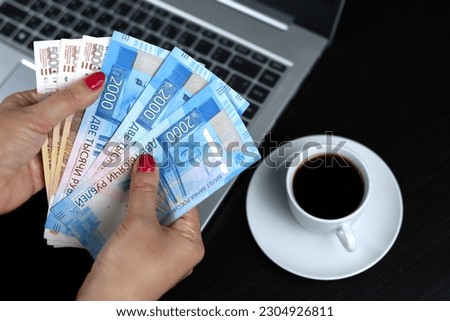 Russian rubles in hands of woman on laptop and coffee cup background. Wages in Russia, bonus or bribe concept