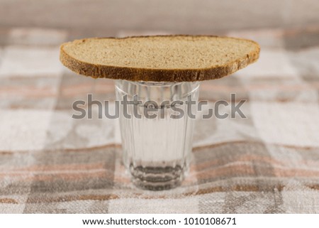 Russian symbol of commemoration of the dead: a loaf of dark rye bread on a full glass of Russian vodka. Wooden table white colors, front view
