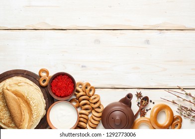 A Russian Tea Party Including Thin Pancake Blini, Red Caviar, Sour Cream And Bagels. Shrovetide Maslenitsa Festival Meal On White Wooden Background. Overhead View With Copy Space