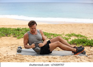 Russian Twist - Fitness Man Exercising On Beach Training With Kettlebells Working Out Core, Obliques And Abdominal Muscles. Male Fitness Instructor Doing Abs Exercise Working Out Six Pack.