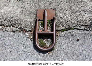 Rusted Broken Fold Down Vehicle Security Car Parking Lock Safety Barrier Mounted On Abandoned Paved Parking Lot On Warm Sunny Summer Day