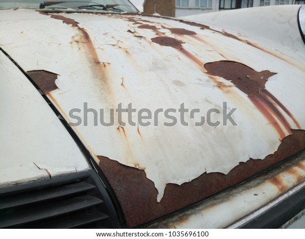 Rusted car hood\
with white chipped car paint\
