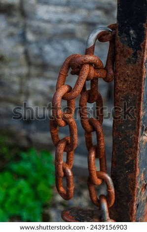 Rusted chain attached to a gate post with peeling paint