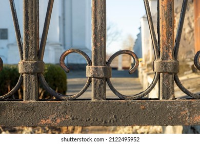 A rusted, decorated, wrought iron fence. Detail of an old retro iron fence made with decorated ironwork elements. Old and rusty iron wrought fence. Coating is peeling off.