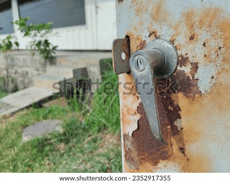 Rusted door handle on metal with rusted and peeling paint. Rusted iron door. Close up of rust metallic door,  bolt handle. Corrosion aged metal panel.