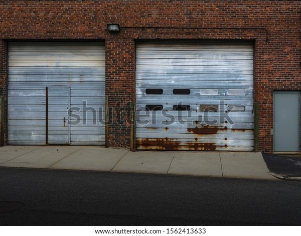 Rusted garage doors in old red brick building on\
paved street