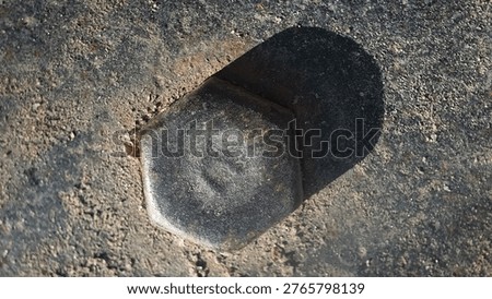 Rusted hexagonal bolt embeds into gritty, weathered concrete surface. Shadow falls sharp and dark beside the corroded metal. Dull, aged steel shows signs of wear and time