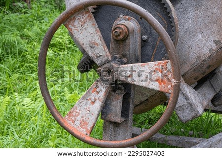 Rusted iron wheel on old cement mixing machine sitting on green grass in Bali, Indonesia