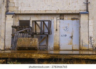 Rusted loading platform with stacked pallets, chained hook, bolted hinges, rotting wood, machine parts, faded markings, industrial service zone left to time